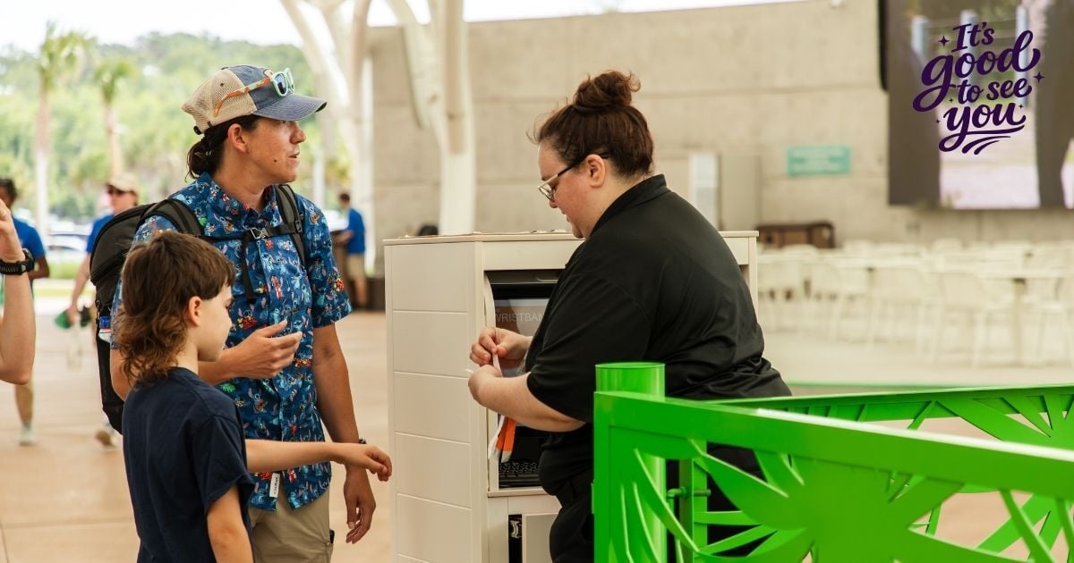 SSA team member assisting a guest and child at an outdoor zoo entrance.